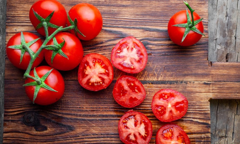 Some tomatoes and slices with knife on a wooden cutting board top view. The fruit that is producing Parkinson’s medication