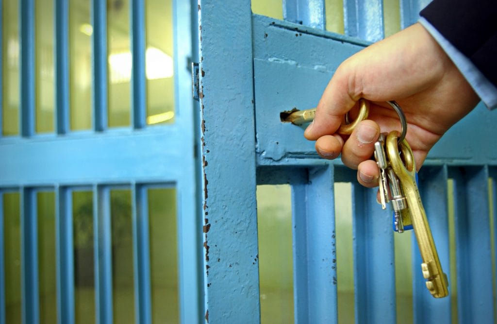 Bright blue cell doors being unlocked by man with a gold set of keys to highlight the problems in the criminal justice system for those with a brain injury