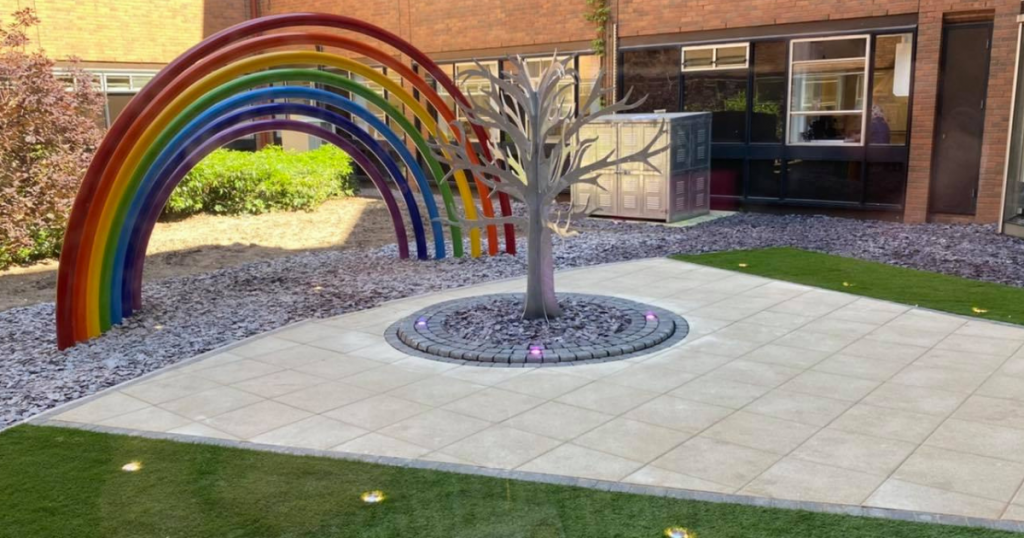 The NHS memory tree marking the death of colleagues stands on a white space with a big rainbow in the background