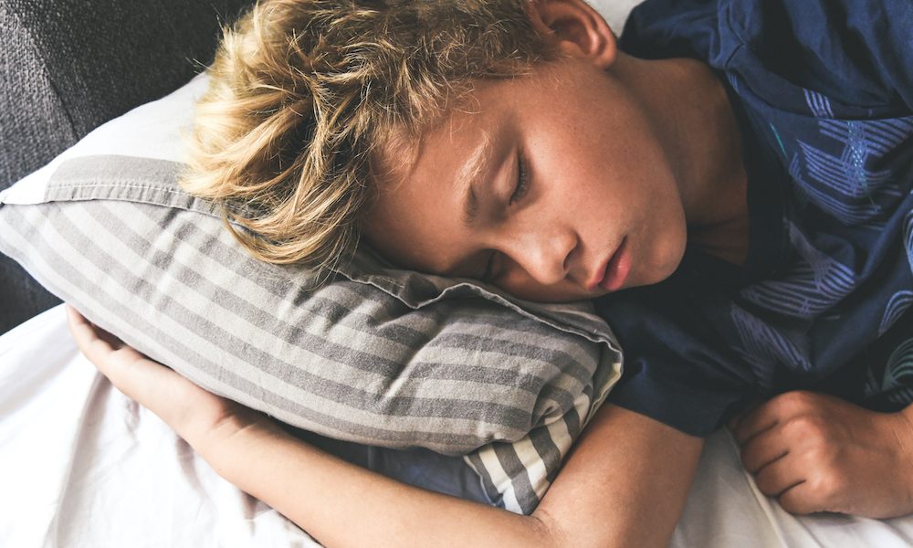 Young boy sleeping with hands on the pillow. Beautiful child sleeps alone in the bed dreaming about vacation. Teen is resting at home pleasantly relaxed. Family, tranquility, serenity carefree concept Sleep and the school summer holidays