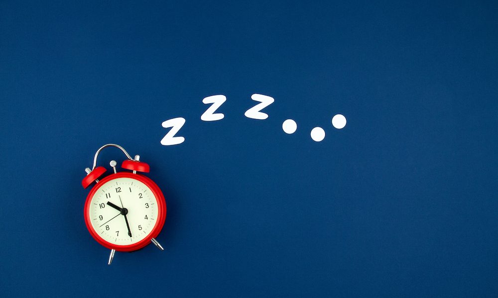 Snoring classic alarm clock on blue pastel trendy background. Flat lay, top view mock up Sleep ‘aids recovery after concussion’