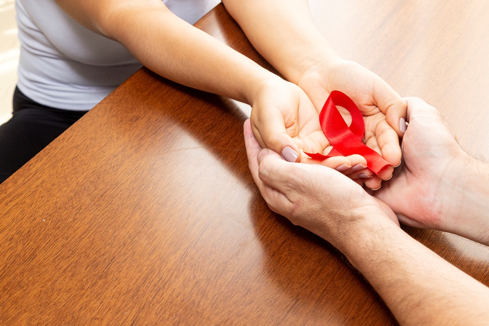 Hands of a couple on the table holding red ribbon. Child brain tumour charity co-founder leaves role